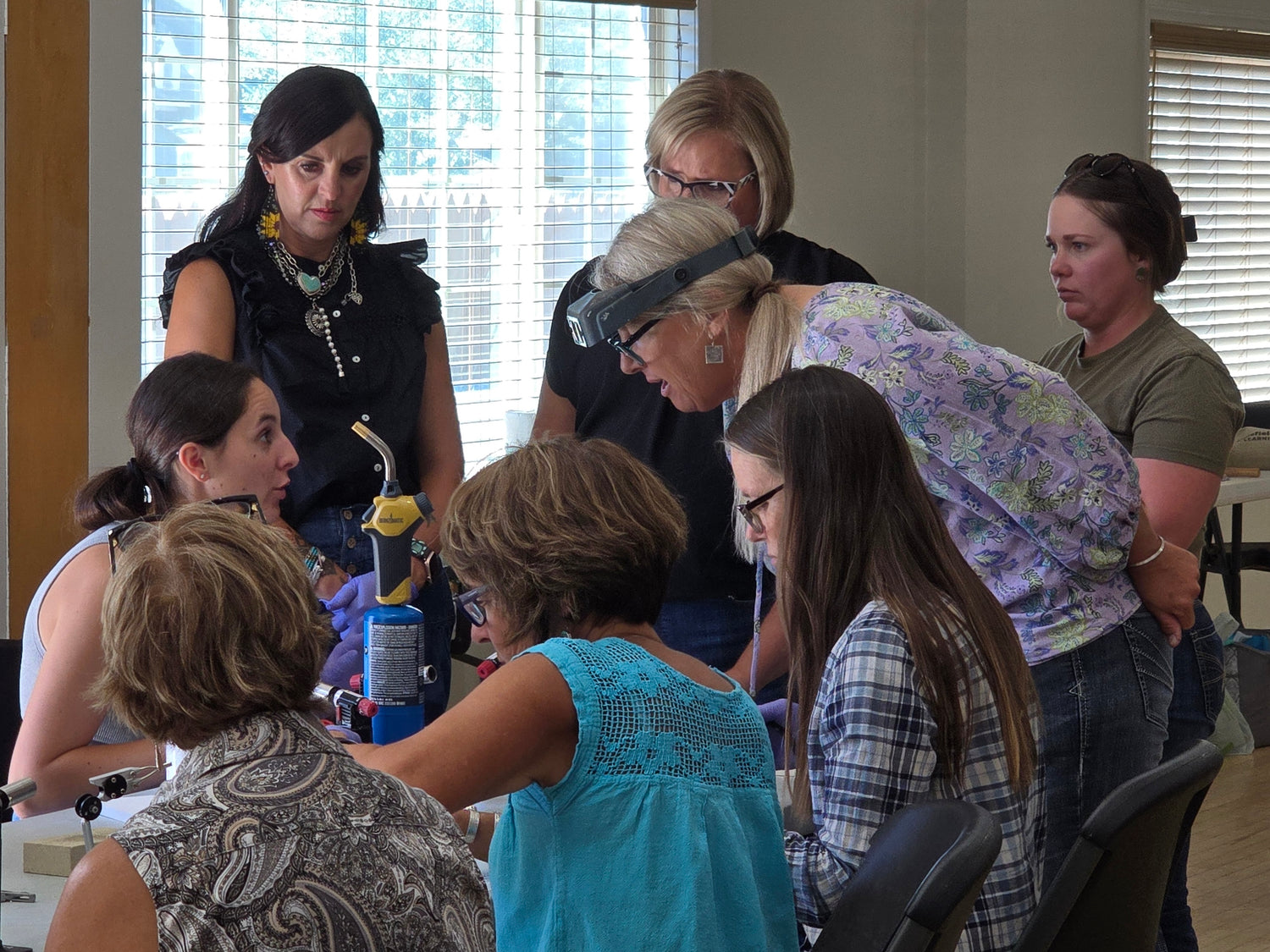Group of women gathered around a table in a room with large windows discussing silversmiting techniques