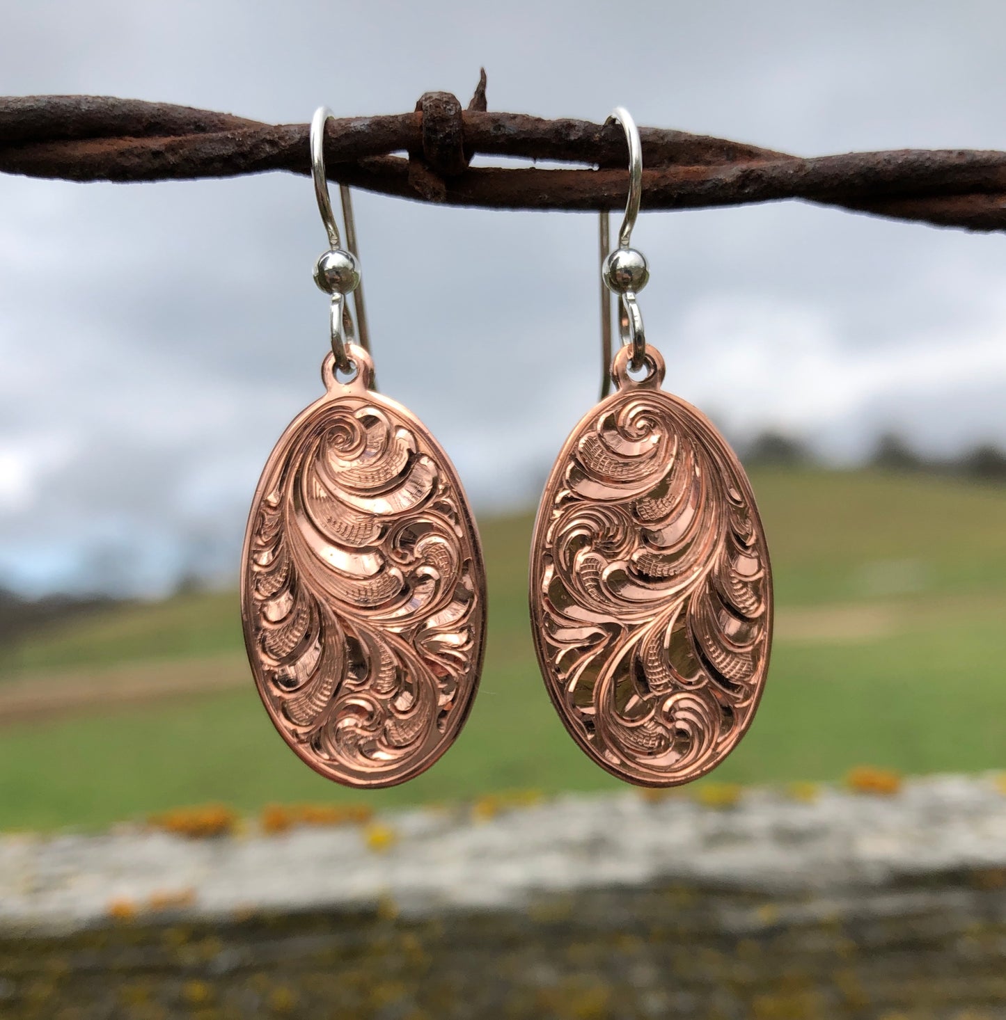 close up of bright cut hand engraved oval copper dangle earrings with sterling silver ear wires
