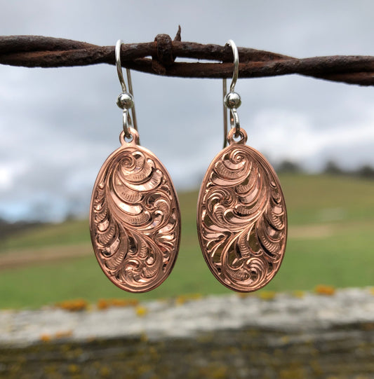 close up of bright cut hand engraved oval copper dangle earrings with sterling silver ear wires 
