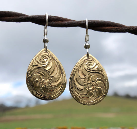 Close up of hand engraved brass teardrop shaped earrings with sterling silver eaer wires