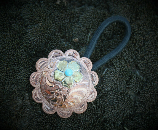 close up of hair concho, beautiful brass flower with turquoise center on a hand engraved copper concho