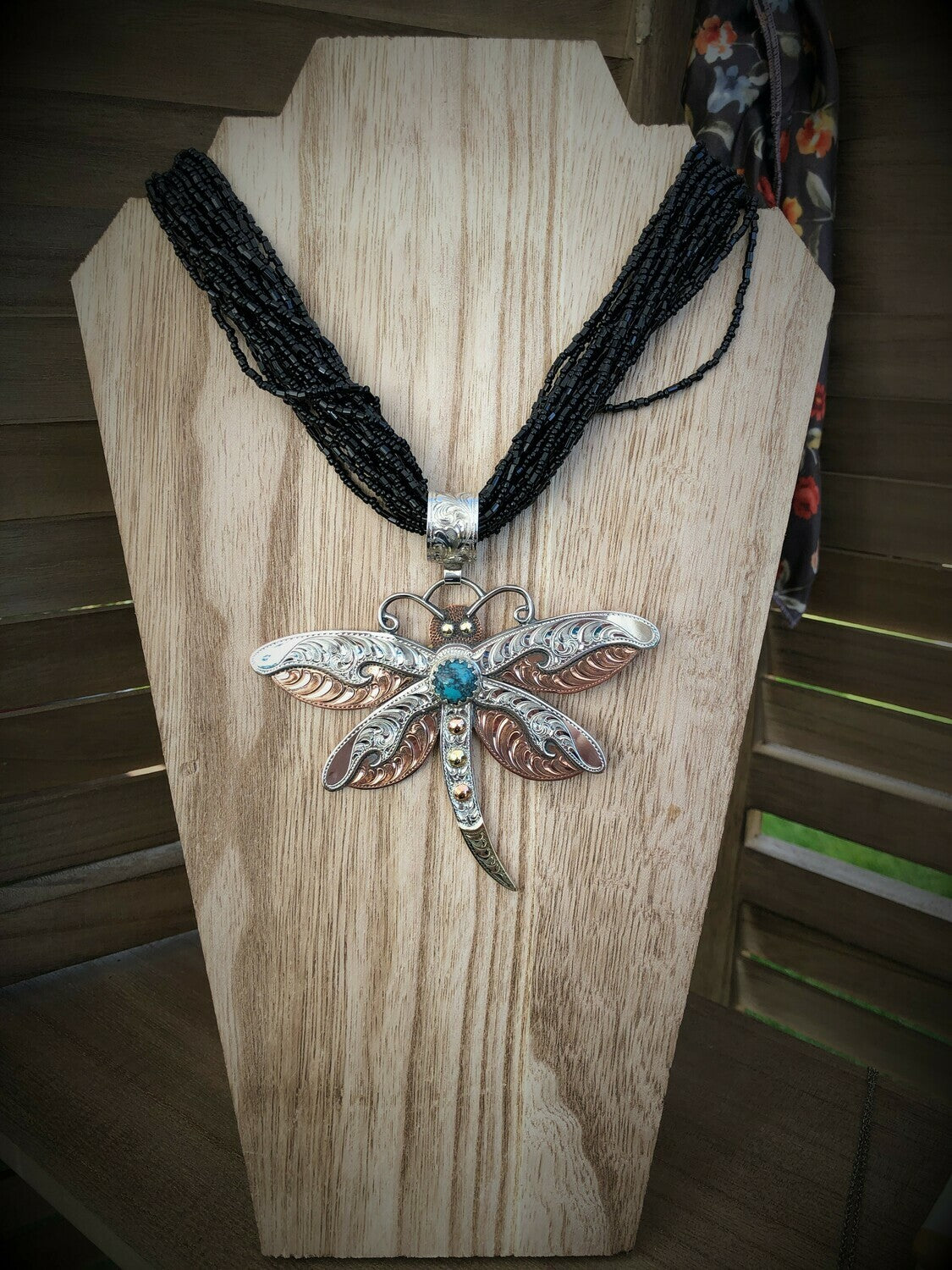 sterling silver dragonfly pendant hanging on a wooden necklace display with a string of black seed beads 